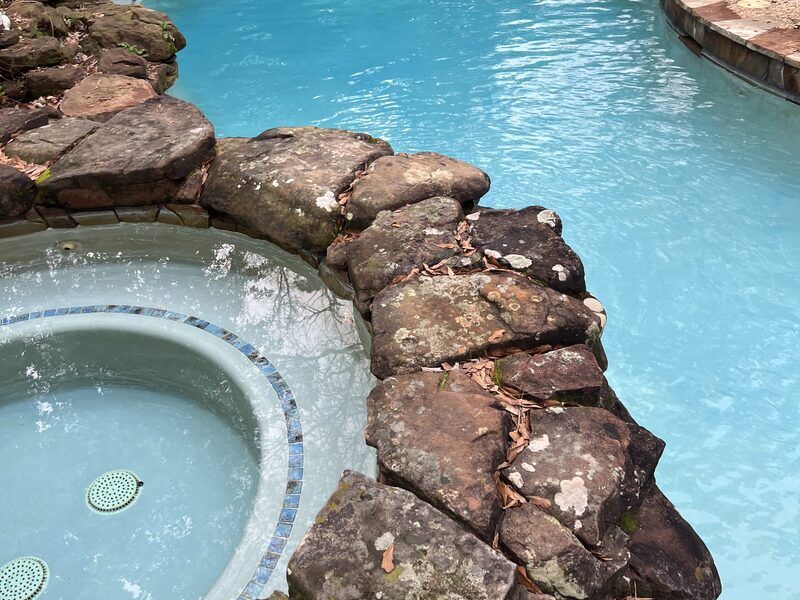 Pool with attached stone spa maintained by Retro Ink Pools